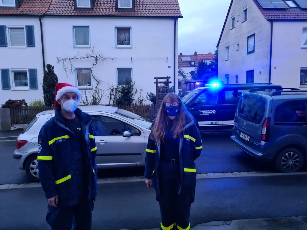 Zwei weihnachtliche THW-Helfer stehen vor einem Fahrzeug mit Blaulicht