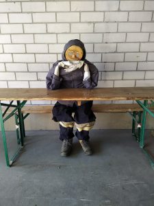 Ein Holz-Dummy sitzt auf einer Bank und schaut in die Kamera