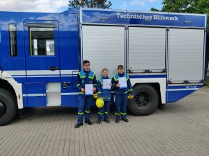 Drei Junghelfer mit Urkunden vor einem GKW.