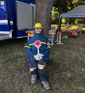 Ein Dummy mit "Holz-Kopf" und Uniform sitzt vor einem Baum.