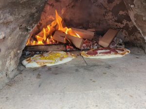 Pizza in einem Lehmofen vor offenen Flammen.