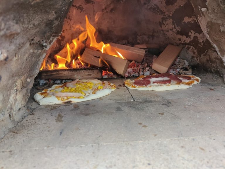 Pizza in einem Lehmofen vor offenen Flammen.
