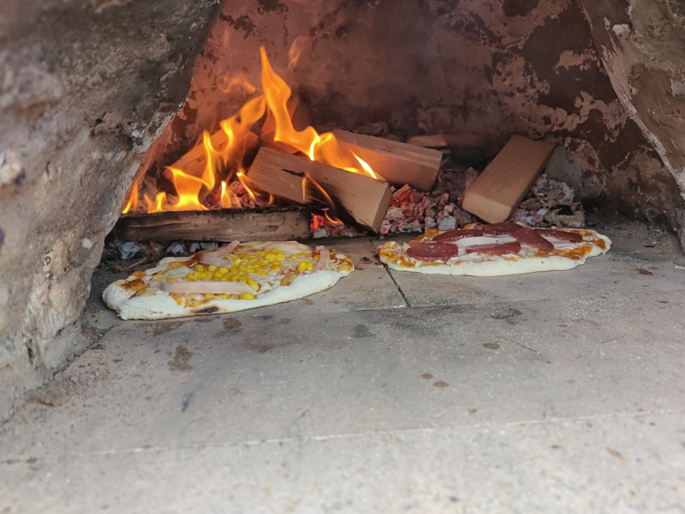 Pizza in einem Lehmofen vor offenen Flammen.