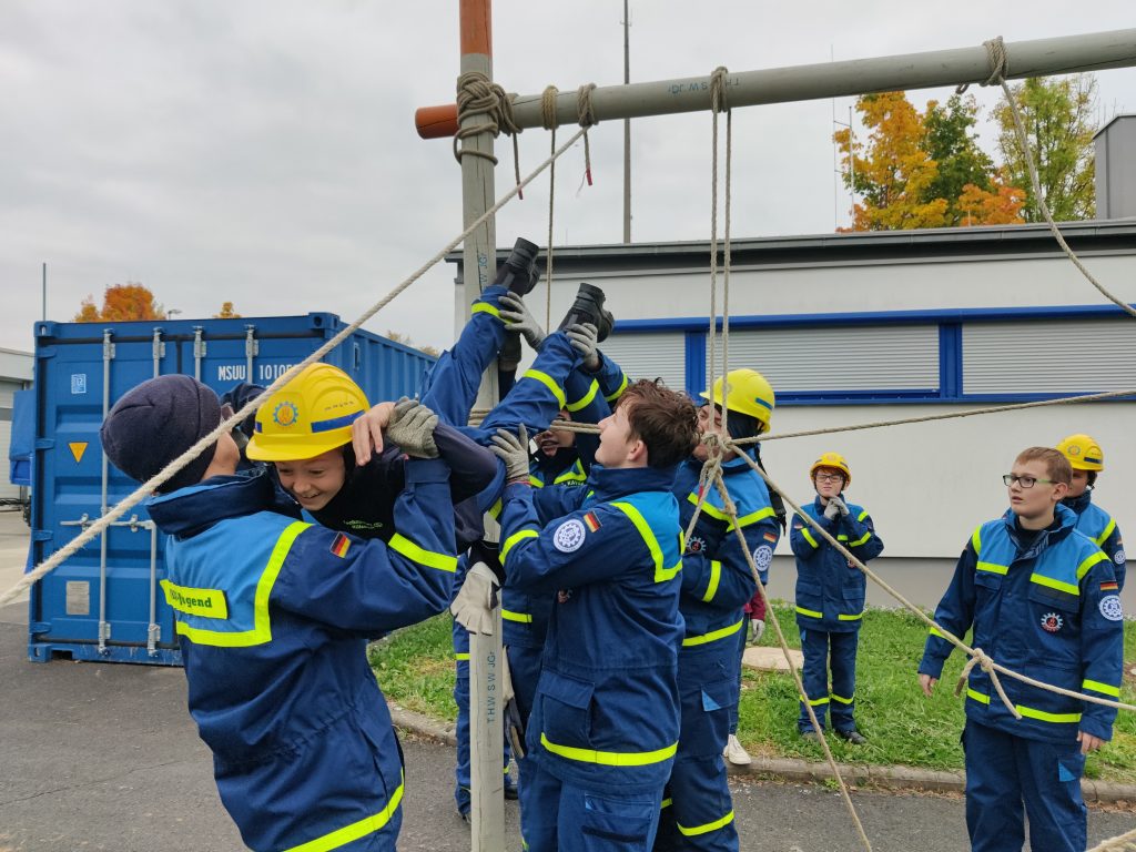 Junghelfer heben einen anderen Junghelfer durch ein Netz aus Leinen
