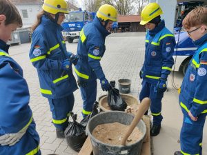 Junghelfer und Teilnehmer der Grundausbildung befüllen gemeinsam Sandsäcke