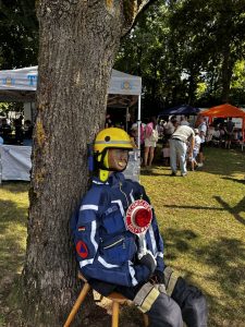 Holzpuppe mit THW-Klamotten lehnt an Baum