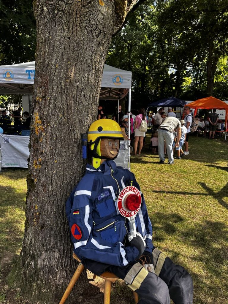 Holzpuppe mit THW-Klamotten lehnt an Baum